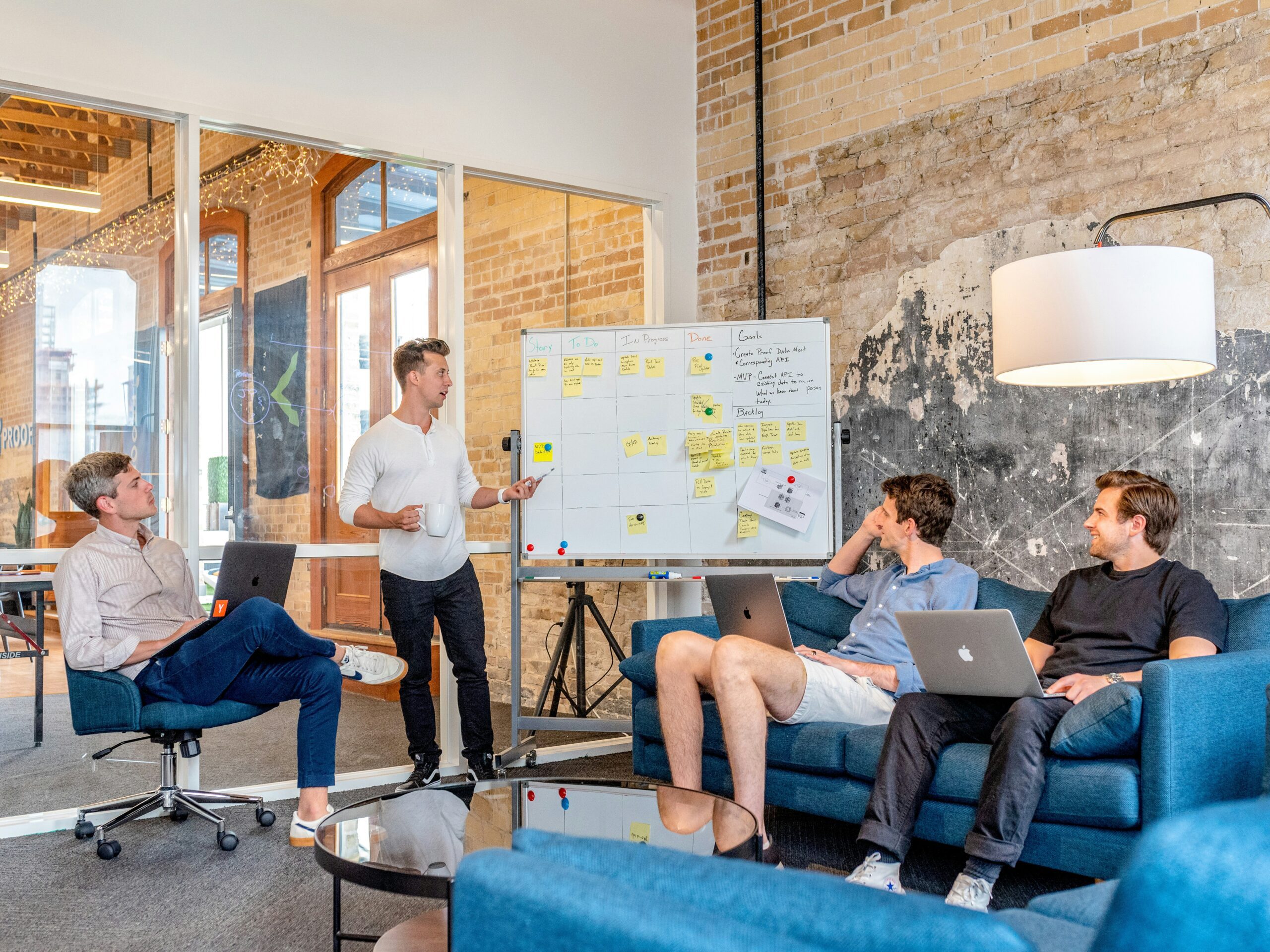 Three men sitting while using laptops and watching man beside whiteboard